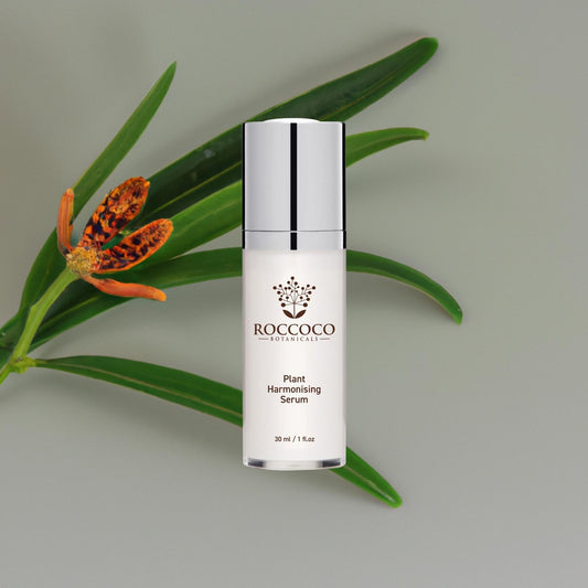 White bottle of Roccoco Botanicals Plant Harmonising Serum on grey background with a flower