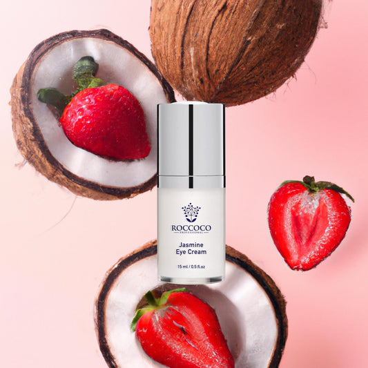 White bottle of Roccoco Jasmine Eye Cream moisturizer on pink background with strawberries and coconuts